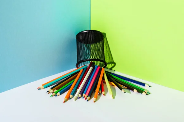 Scattered colored pencils from pencil holder on blue, green and white background — Stock Photo