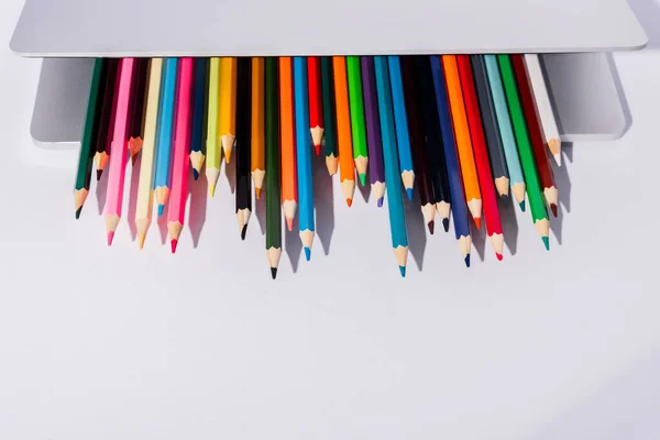 Lápis coloridos no laptop moderno no fundo branco — Fotografia de Stock