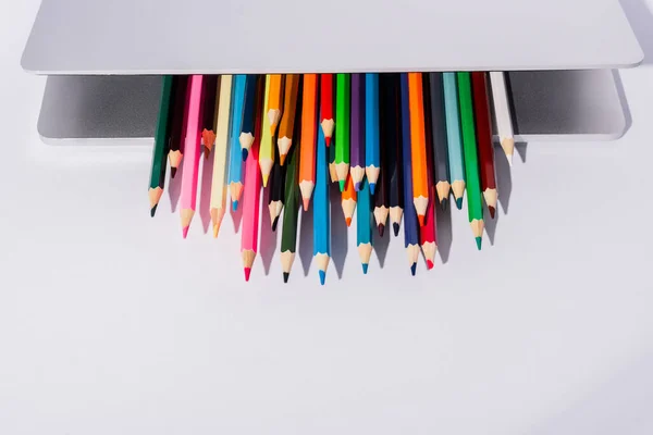 Lápis coloridos no laptop moderno no fundo branco — Fotografia de Stock