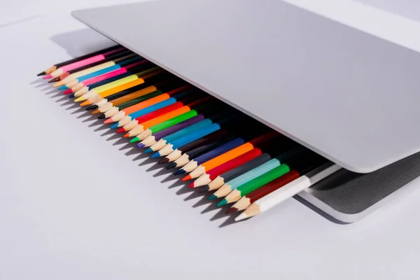 Crayons de couleur dans un ordinateur portable moderne sur fond blanc — Photo de stock