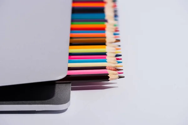 Mise au point sélective de crayons de couleur dans un ordinateur portable moderne sur fond blanc — Photo de stock