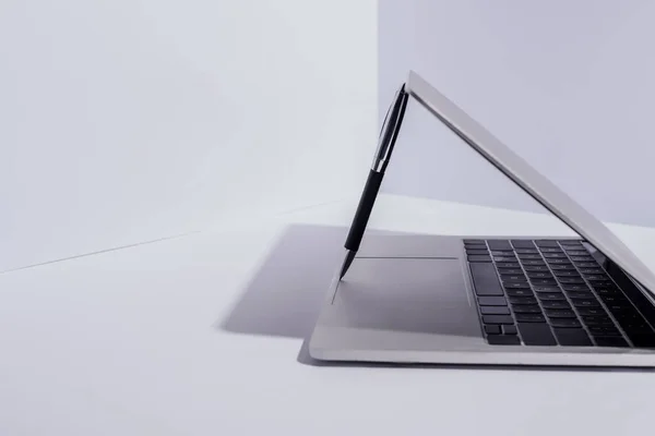 Caneta no laptop moderno no fundo branco — Fotografia de Stock