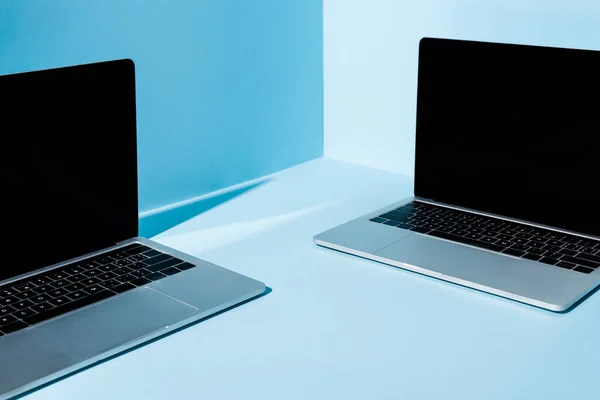Moderne Laptops mit leeren Bildschirmen auf blauem Hintergrund — Stockfoto