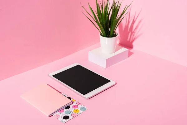Tableta digital con pantalla en blanco, cuadernos, planta sobre fondo rosa - foto de stock