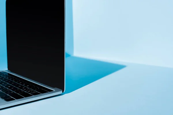 Modern laptop with blank screen at blue workplace in light — Stock Photo