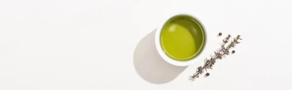 Vue du dessus de l'huile d'olive dans un bol près de l'herbe et du poivre noir sur fond blanc, orientation panoramique — Photo de stock