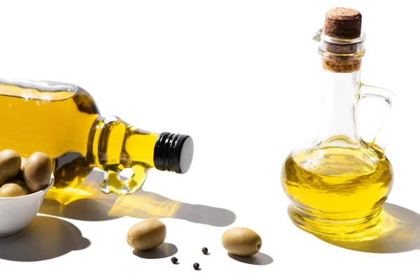 Оливковое масло в бутылках рядом с зелеными оливками и черный перец на белом фоне — стоковое фото