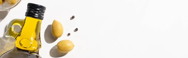 Top view of olive oil in bottle near green olives and black pepper on white background, panoramic orientation — Stock Photo