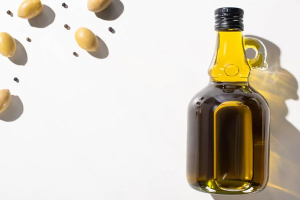 Top view of olive oil in bottle near green olives and black pepper on white background — Stock Photo