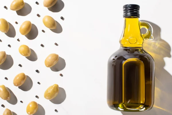 Top view of olive oil in bottle near green olives and black pepper on white background — Stock Photo