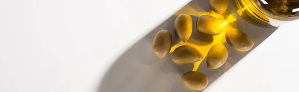 Vue du dessus de l'huile d'olive en bouteille près des olives vertes à l'ombre sur fond blanc, orientation panoramique — Photo de stock