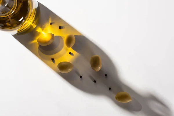 Top view of olive oil in bottle near green olives and black pepper in shadow on white background — Stock Photo