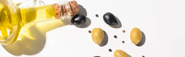 Vue du dessus de l'huile d'olive en bouteille près des olives vertes et noires et du poivre noir sur fond blanc avec ombre, orientation panoramique — Photo de stock