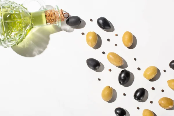 Ansicht von Olivenöl in der Flasche in der Nähe von grünen und schwarzen Oliven und schwarzem Pfeffer auf weißem Hintergrund mit Schatten — Stockfoto