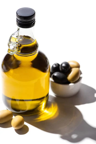 Aceite de oliva en botella cerca de aceitunas verdes y negras en tazón sobre fondo blanco - foto de stock
