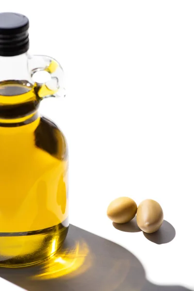 Оливковое масло в бутылке возле зеленых оливок на белом фоне — стоковое фото