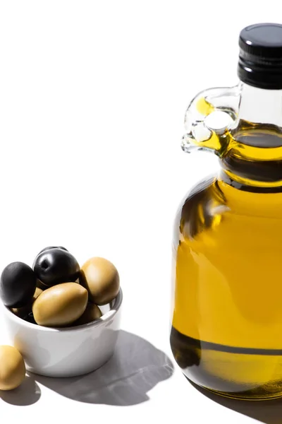 Olio di oliva in bottiglia vicino olive verdi e nere in ciotola su fondo bianco — Foto stock