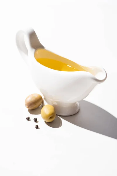 Olive oil in gravy boat near green olives and black pepper on white background — Stock Photo