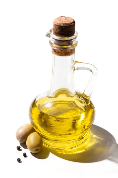 Aceite de oliva en frasco cerca de aceitunas verdes y pimienta negra sobre fondo blanco - foto de stock