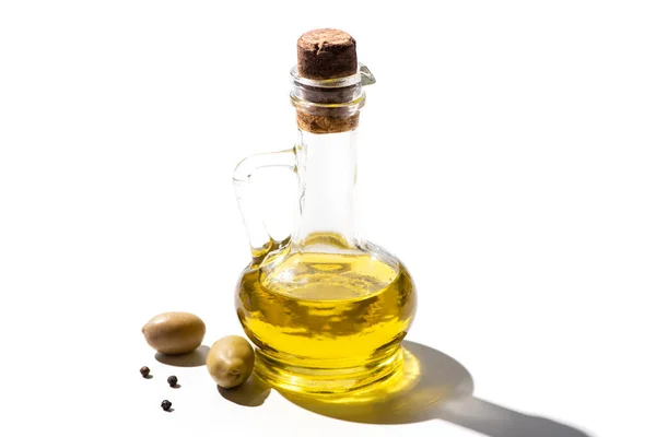 Оливковое масло в банке рядом с зелеными оливками и черный перец на белом фоне — стоковое фото