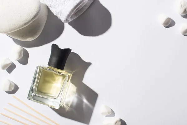 Vista superior de varas de aroma com perfume em garrafa perto de pedras de spa e toalha no fundo branco — Fotografia de Stock