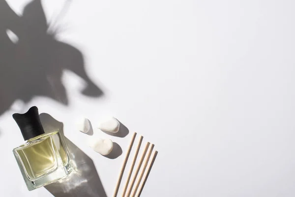 Вид сверху ароматных палочек с духами в бутылке рядом с камнями на белом фоне — стоковое фото