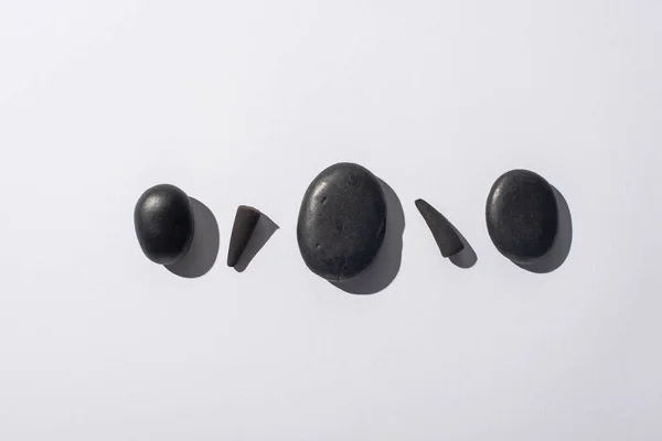 Vista superior de conos de incienso negro y piedras de spa sobre fondo blanco - foto de stock