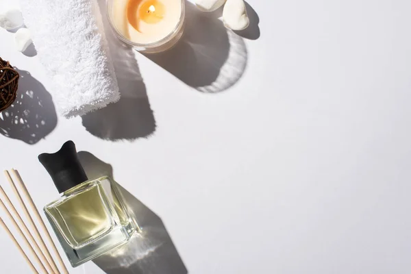 Vista dall'alto di bastoncini aroma con profumo in bottiglia vicino asciugamano di cotone, pietre e candela su sfondo bianco — Foto stock