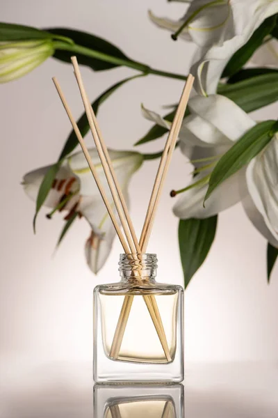 Selektiver Fokus von Holzstäbchen im Parfüm in der Flasche in der Nähe von Lilienblüten auf beigem Hintergrund — Stockfoto
