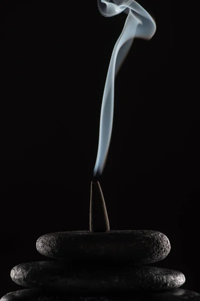 Burning incense cone with smoke on stones on black background — Stock Photo