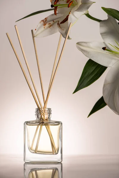 Holzstäbchen im Parfüm in der Flasche in der Nähe von Lilienblüten auf beigem Hintergrund — Stockfoto