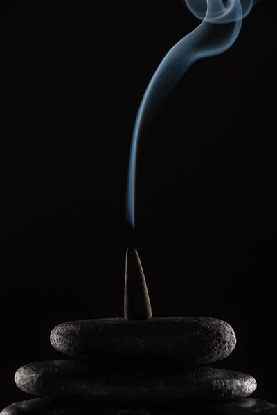Burning incense cone with smoke on stones on black background — Stock Photo