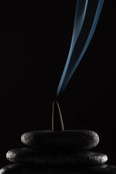 Cône d'encens brûlant avec de la fumée sur des pierres sur fond noir — Photo de stock
