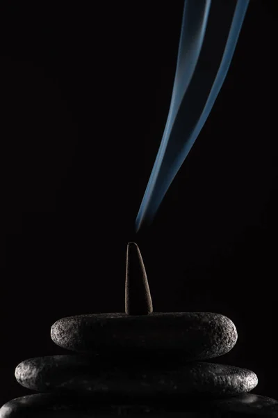 Burning incense cone with smoke on stones on black background — Stock Photo