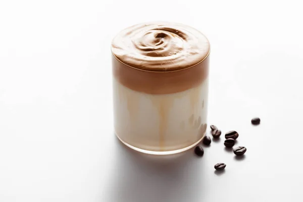 Délicieux café Dalgona en verre près des grains de café sur fond blanc — Photo de stock