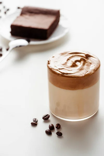 Вибірковий фокус смачної кави Далгони в склянці біля кавових зерен на білому фоні — стокове фото