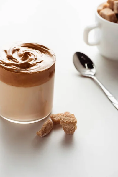 Вибірковий фокус смачної кави Далгони в склянці поблизу ложки і коричневого цукру на білому тлі — стокове фото