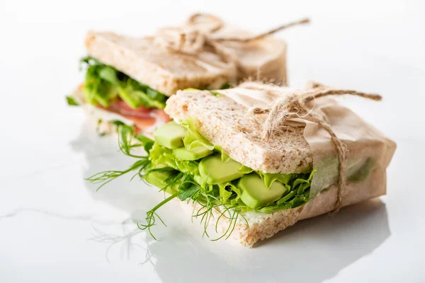 Selective focus of fresh green sandwiches with avocado on marble white surface — Stock Photo