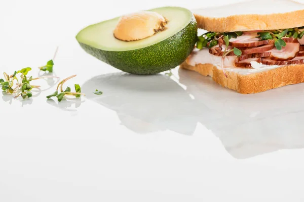 Sanduíche delicioso fresco com carne e brotos na superfície branca perto do abacate — Fotografia de Stock