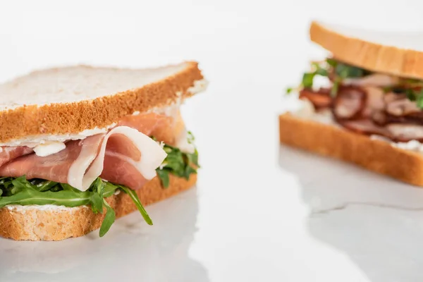 Foco seletivo de sanduíche fresco com arugula e prosciutto na superfície branca de mármore — Fotografia de Stock