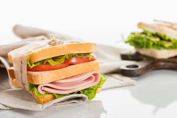 Delicioso sándwich fresco con salchicha en rodajas y lechuga en la servilleta en la superficie blanca - foto de stock