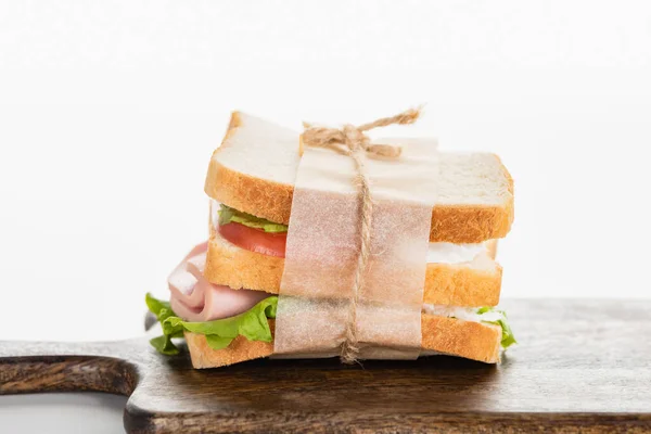 Sanduíche delicioso fresco com salsicha fatiada e alface em tábua de corte de madeira na superfície branca — Fotografia de Stock