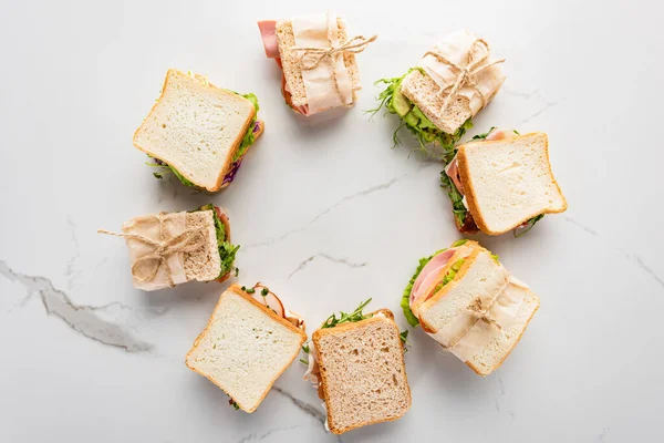 Top view of fresh sandwiches arranged in round frame on marble white surface — Stock Photo