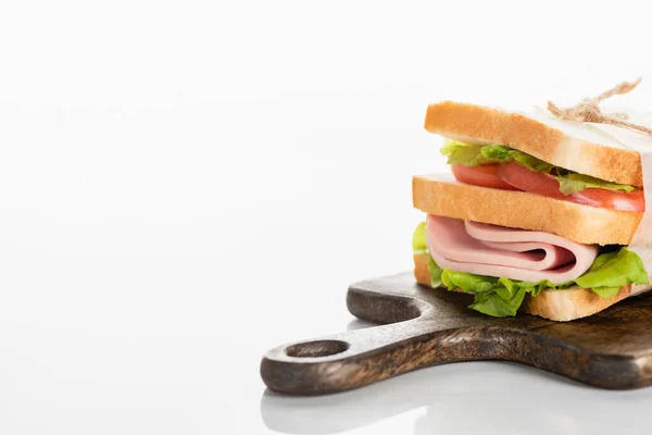 Delicioso sándwich fresco con salchicha en rodajas y lechuga en tabla de cortar de madera en la superficie blanca - foto de stock