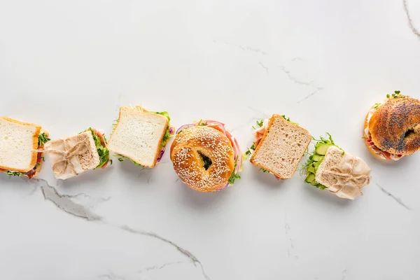 Leigos planos com sanduíches frescos e bagels na superfície branca de mármore — Fotografia de Stock