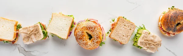 Tendido plano con sándwiches frescos y rosquillas en la superficie blanca de mármol, plano panorámico - foto de stock