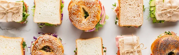 Leigos planos com sanduíches frescos e bagels na superfície branca de mármore, tiro panorâmico — Fotografia de Stock