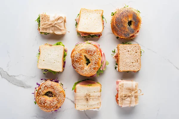 Leigos planos com sanduíches frescos e bagels na superfície branca de mármore — Fotografia de Stock