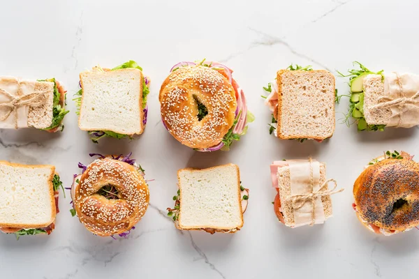 Leigos planos com sanduíches frescos e bagels na superfície branca de mármore — Fotografia de Stock