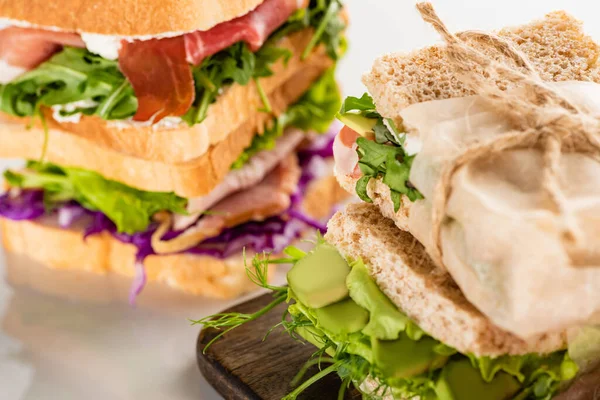 Mise au point sélective de sandwichs frais avec viande sur planche à découper en bois sur surface blanche — Photo de stock